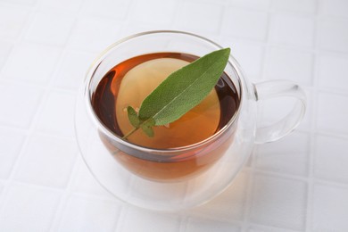 Aromatic herbal tea with sage in cup on white tiled table