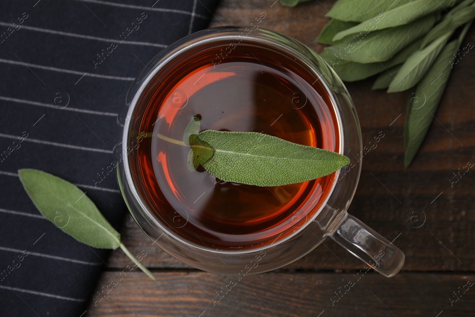 Photo of Aromatic herbal tea in cup with sage on wooden table, top view