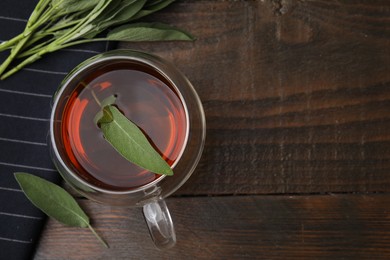 Aromatic herbal tea in cup with sage on wooden table, top view. Space for text