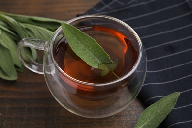 Aromatic herbal tea in cup with sage on wooden table, closeup