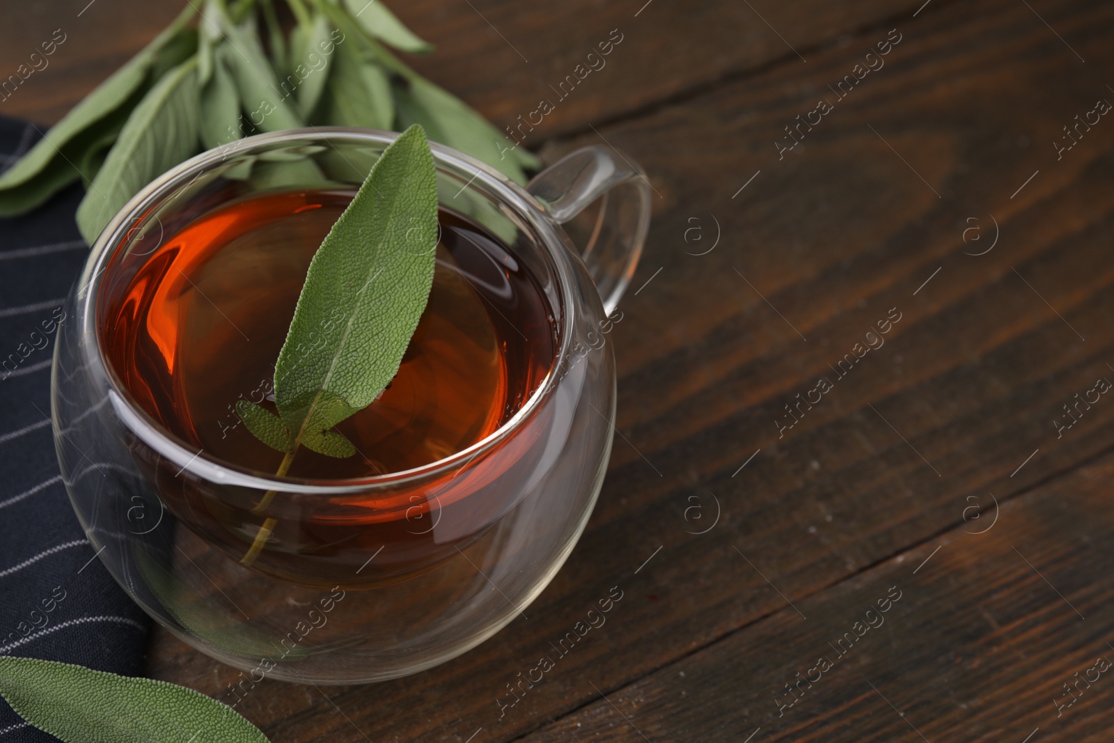 Photo of Aromatic herbal tea in cup with sage on wooden table, space for text