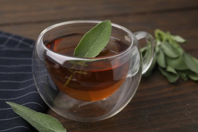 Aromatic herbal tea in cup with sage on wooden table, closeup