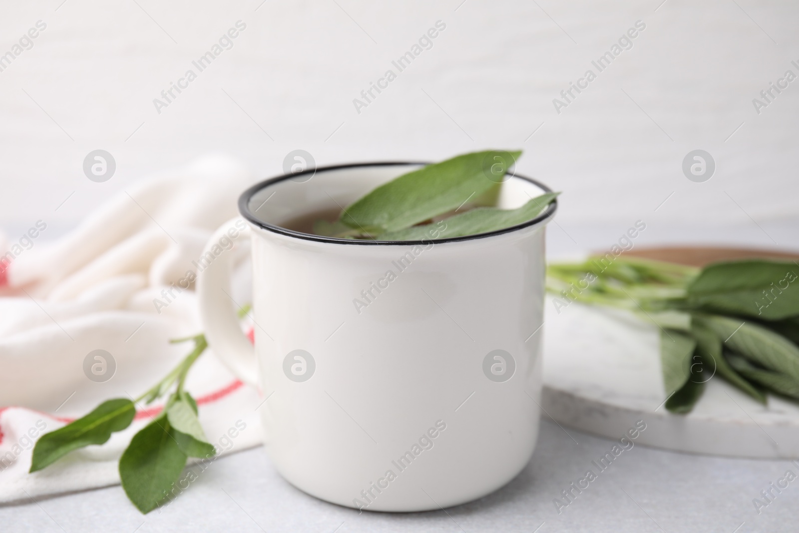 Photo of Aromatic herbal tea in mug with sage on light table, closeup