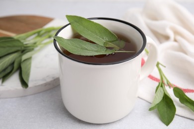 Photo of Aromatic herbal tea in mug with sage on light table, closeup