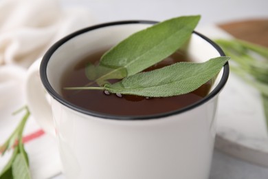 Aromatic herbal tea in mug with sage on light table, closeup