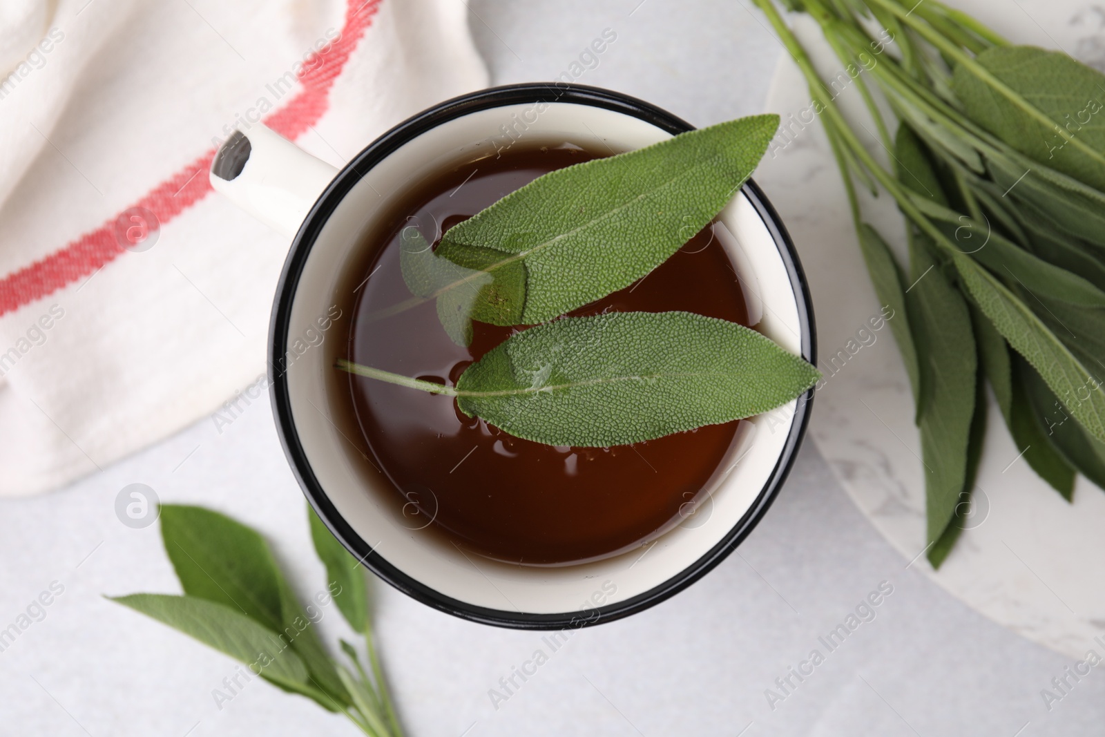 Photo of Aromatic herbal tea in mug with sage on light table, top view