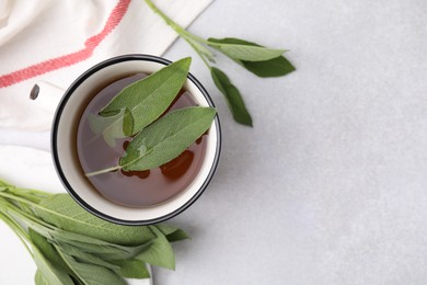 Photo of Aromatic herbal tea in mug with sage on light table, top view. Space for text