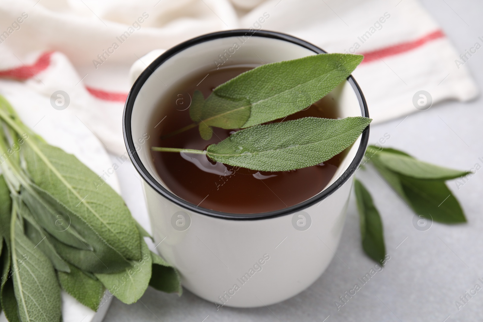 Photo of Aromatic herbal tea in mug with sage on light table, closeup