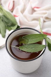 Aromatic herbal tea in mug with sage on light table, closeup