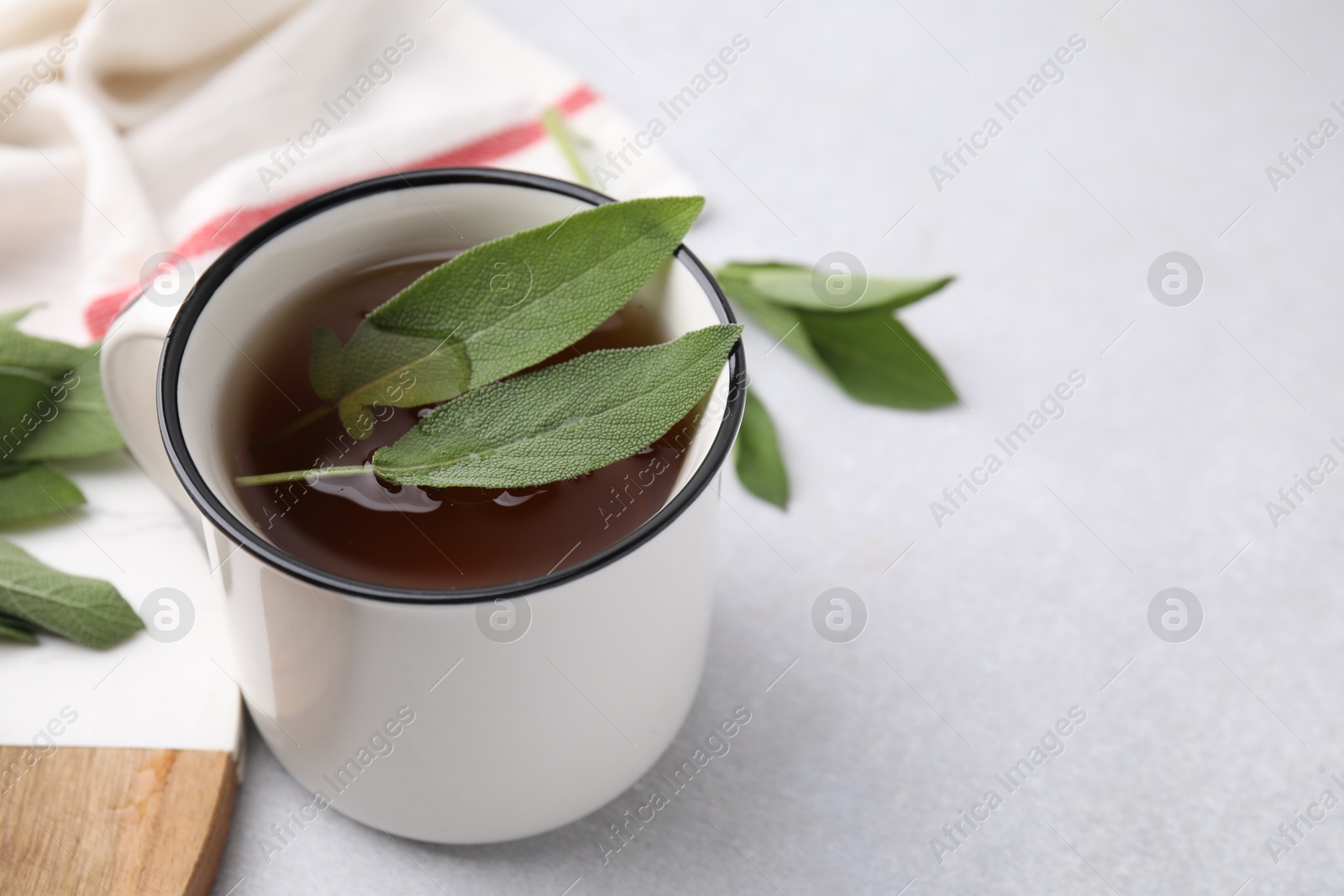 Photo of Aromatic herbal tea in mug with sage on light table, closeup. Space for text