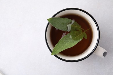 Aromatic herbal tea with sage in mug on light table, top view. Space for text