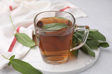 Photo of Aromatic herbal tea in cup with sage on white table, closeup