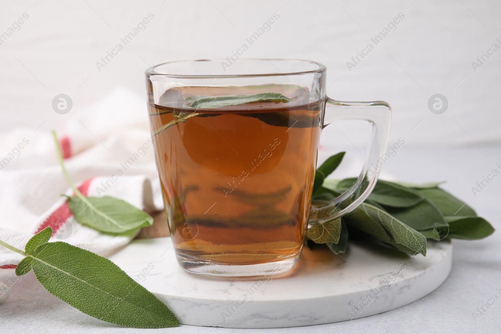 Photo of Aromatic herbal tea in cup with sage on white table, closeup