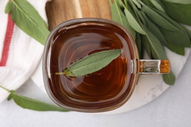 Aromatic herbal tea in cup with sage on white table, top view