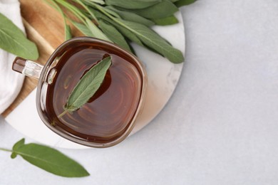 Aromatic herbal tea in cup with sage on light table, top view. Space for text