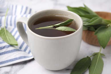 Photo of Aromatic herbal tea in cup with sage on white table, closeup