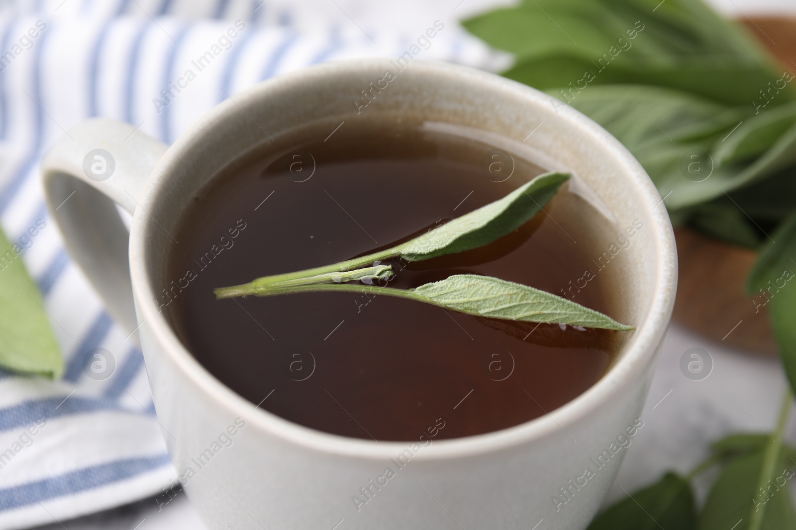 Photo of Aromatic herbal tea in cup with sage on white table, closeup