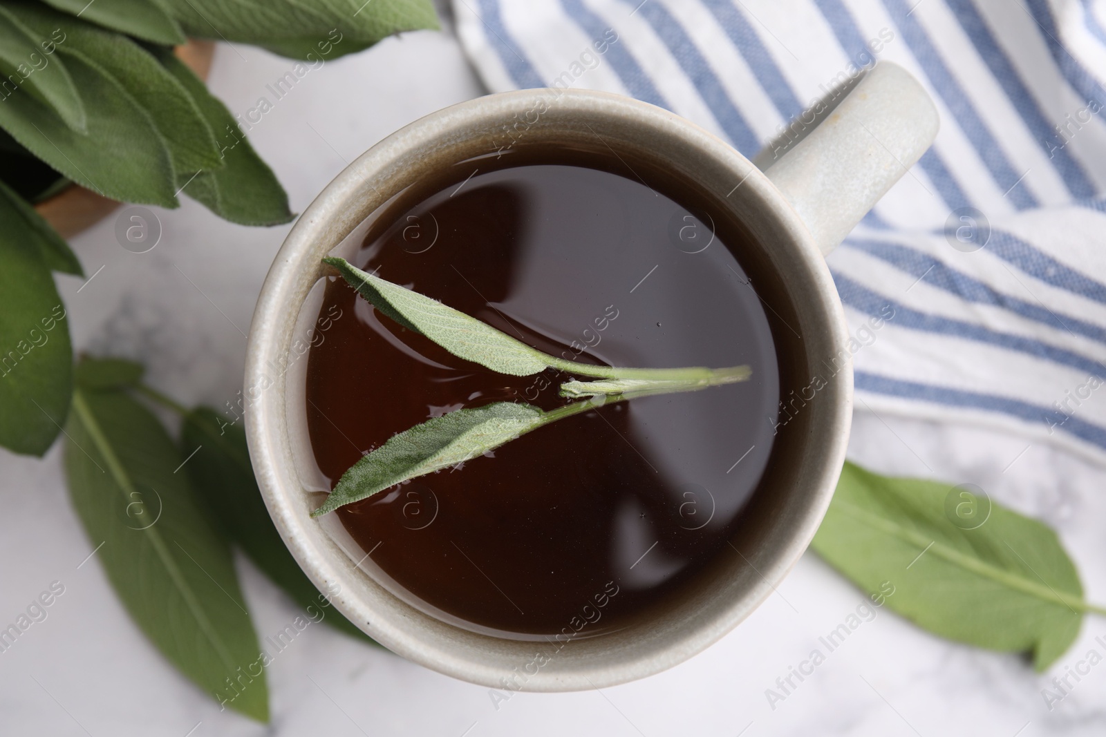 Photo of Aromatic herbal tea in cup with sage on white table, top view