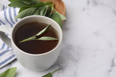 Aromatic herbal tea in cup with sage on white marble table, space for text