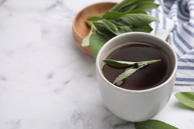 Photo of Aromatic herbal tea in cup with sage on white marble table, space for text