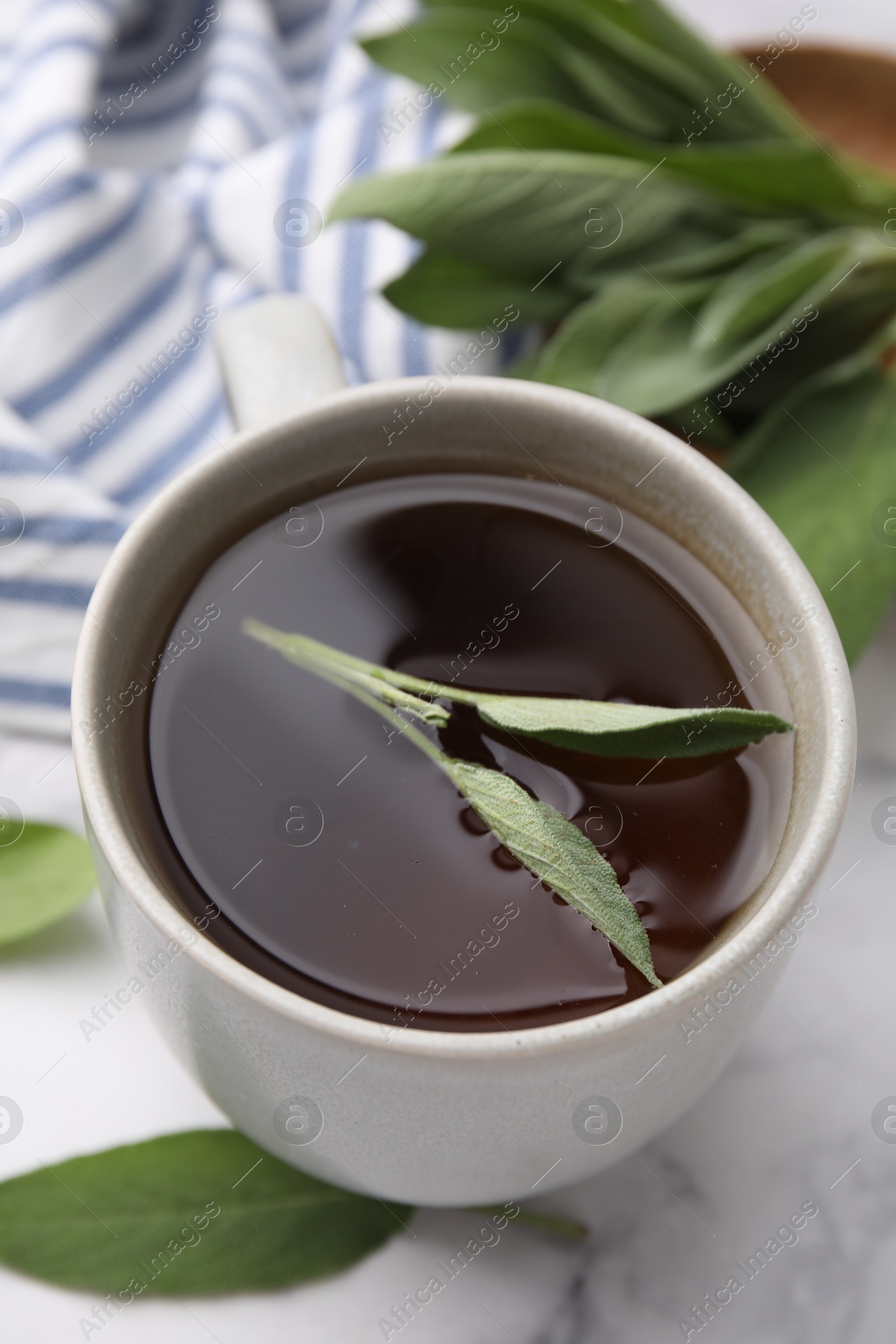 Photo of Aromatic herbal tea in cup with sage on white marble table