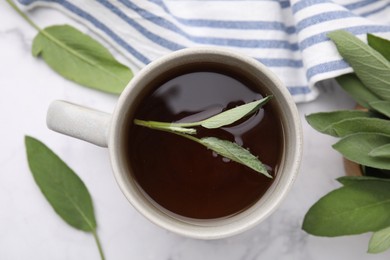 Aromatic herbal tea in cup with sage on white marble table, top view