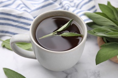 Aromatic herbal tea in cup with sage on white marble table