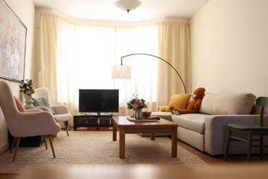 Photo of Cozy living room with modern furniture, TV set and bouquets of flowers. Interior design