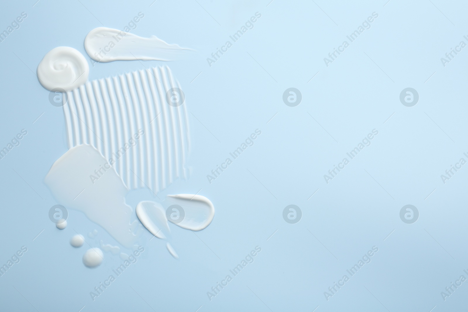 Photo of Samples of face cream on light blue background, top view. Space for text