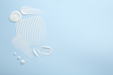 Photo of Samples of face cream on light blue background, top view. Space for text