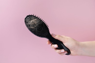 Woman holding brush with lost hair on pink background, closeup