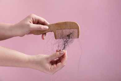 Photo of Woman taking her lost hair from comb on pink background, closeup. Space for text