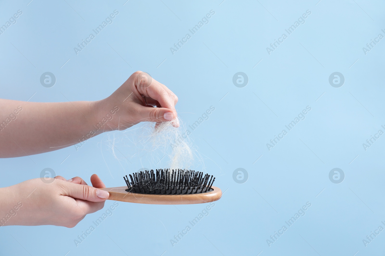 Photo of Woman taking her lost hair from brush on light blue background, closeup. Space for text