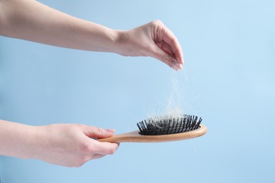 Photo of Woman taking her lost hair from brush on light blue background, closeup