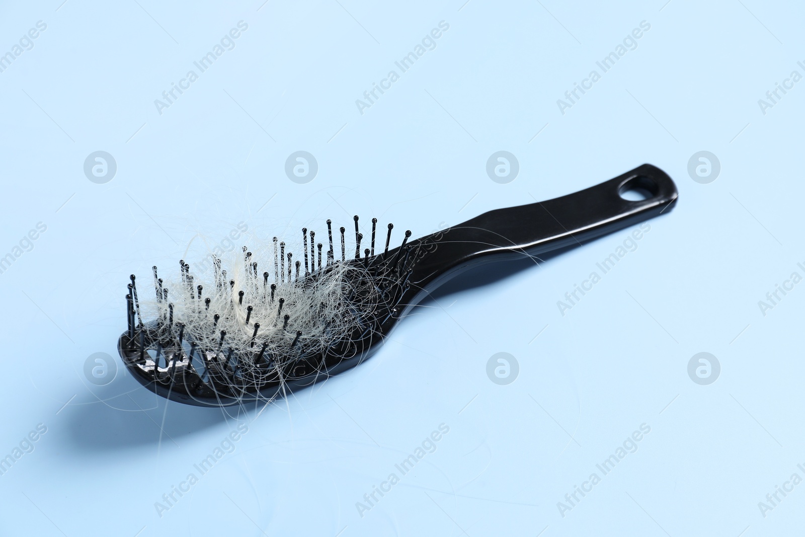 Photo of Brush with lost hair on light blue background