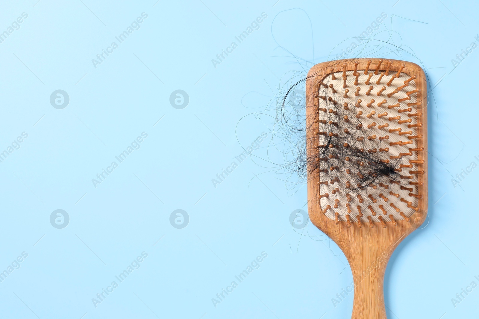 Photo of Wooden brush with lost hair on light blue background, top view. Space for text