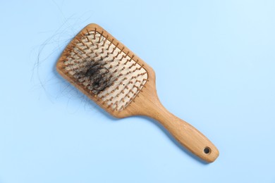 Wooden brush with lost hair on light blue background, top view