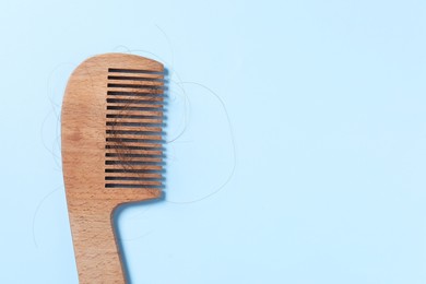 Photo of Wooden comb with lost hair on light blue background, top view. Space for text