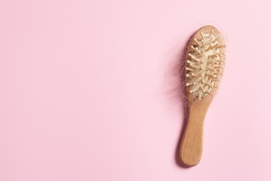 Photo of Wooden brush with lost hair on pink background, top view. Space for text