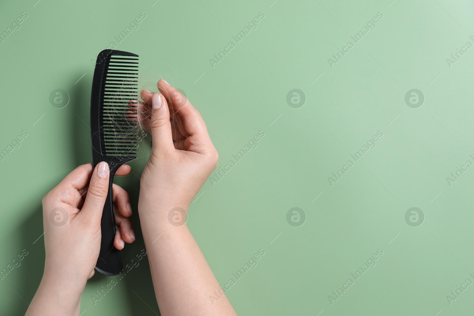 Photo of Woman taking her lost hair from comb on green background, top view. Space for text