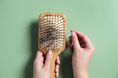 Photo of Woman holding brush with lost hair on green background, top view