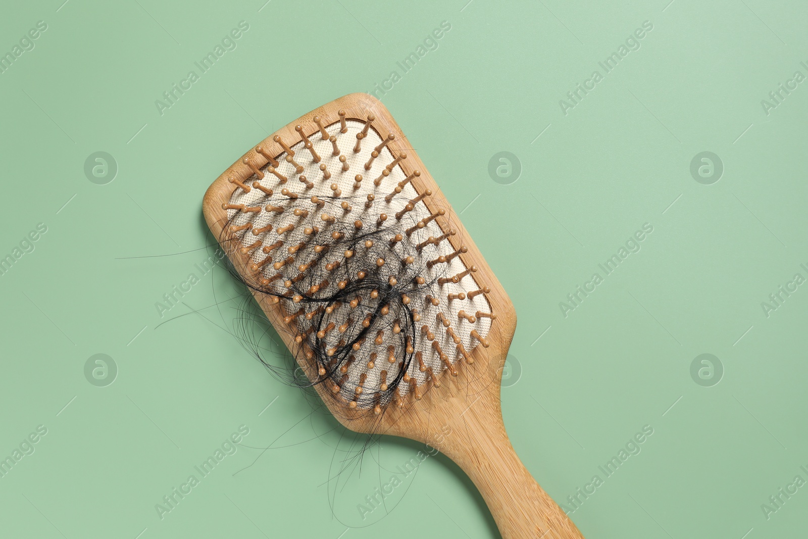 Photo of Wooden brush with lost hair on green background, top view