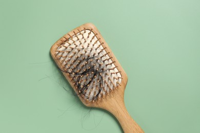 Wooden brush with lost hair on green background, top view