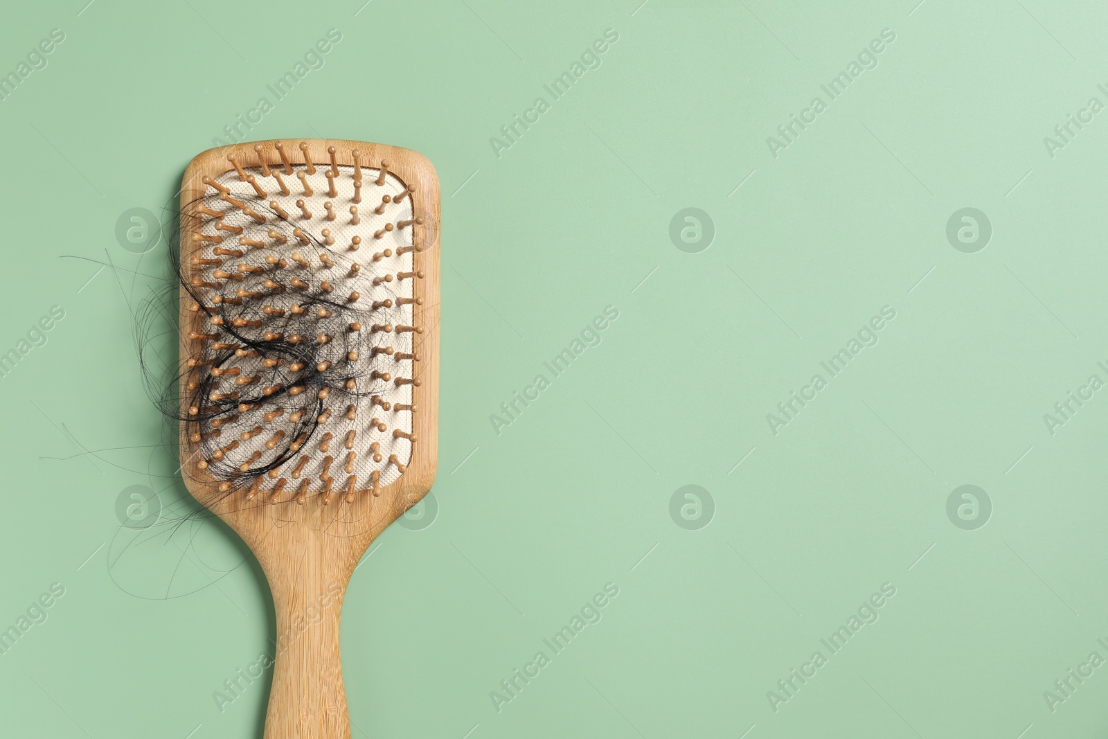 Photo of Wooden brush with lost hair on green background, top view. Space for text