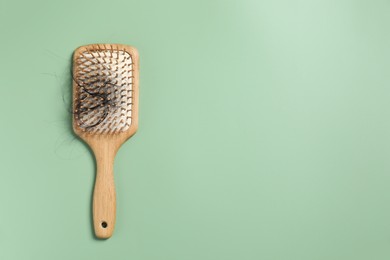 Wooden brush with lost hair on green background, top view. Space for text