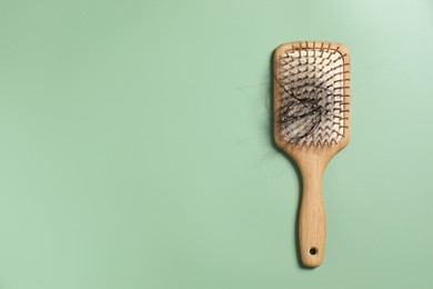 Wooden brush with lost hair on green background, top view. Space for text