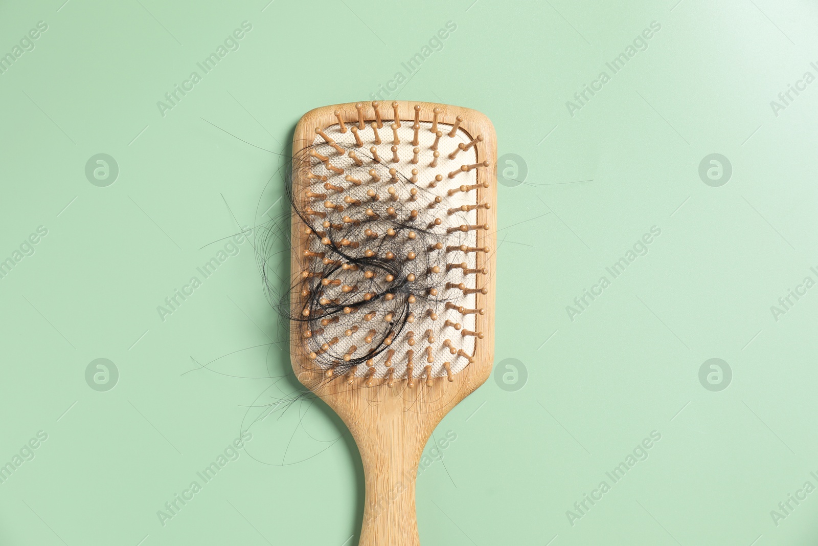 Photo of Wooden brush with lost hair on green background, top view