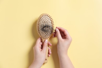 Photo of Woman holding brush with lost hair on yellow background, top view