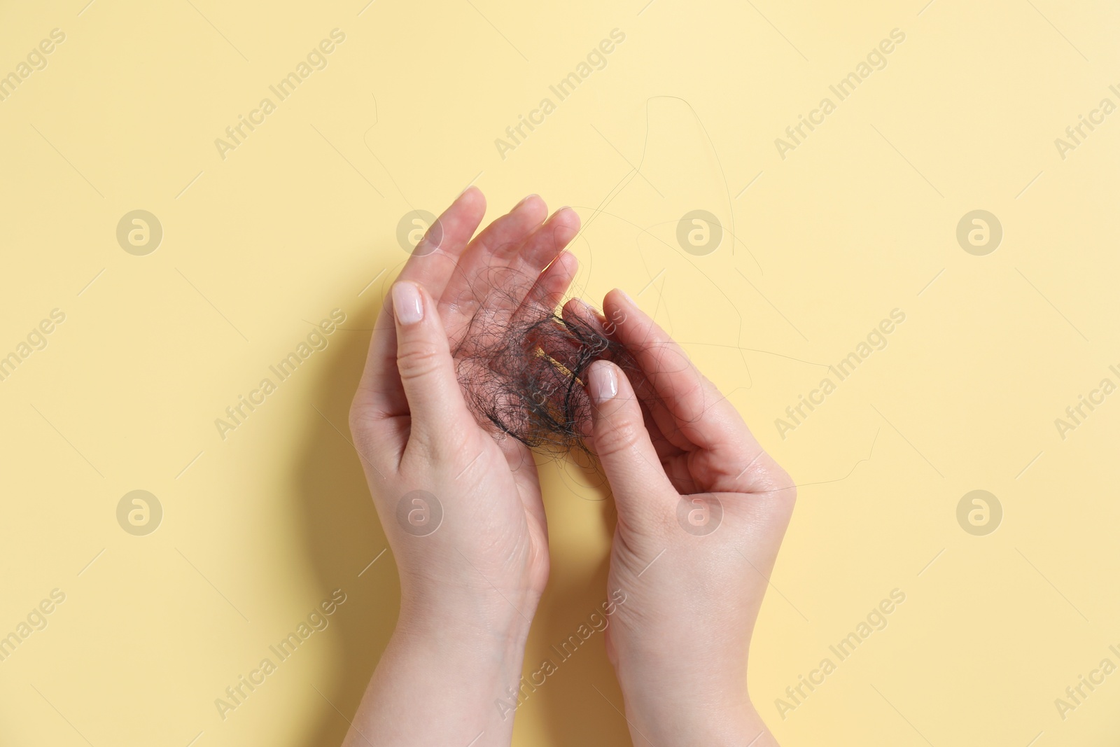 Photo of Woman holding her lost hair on yellow background, top view