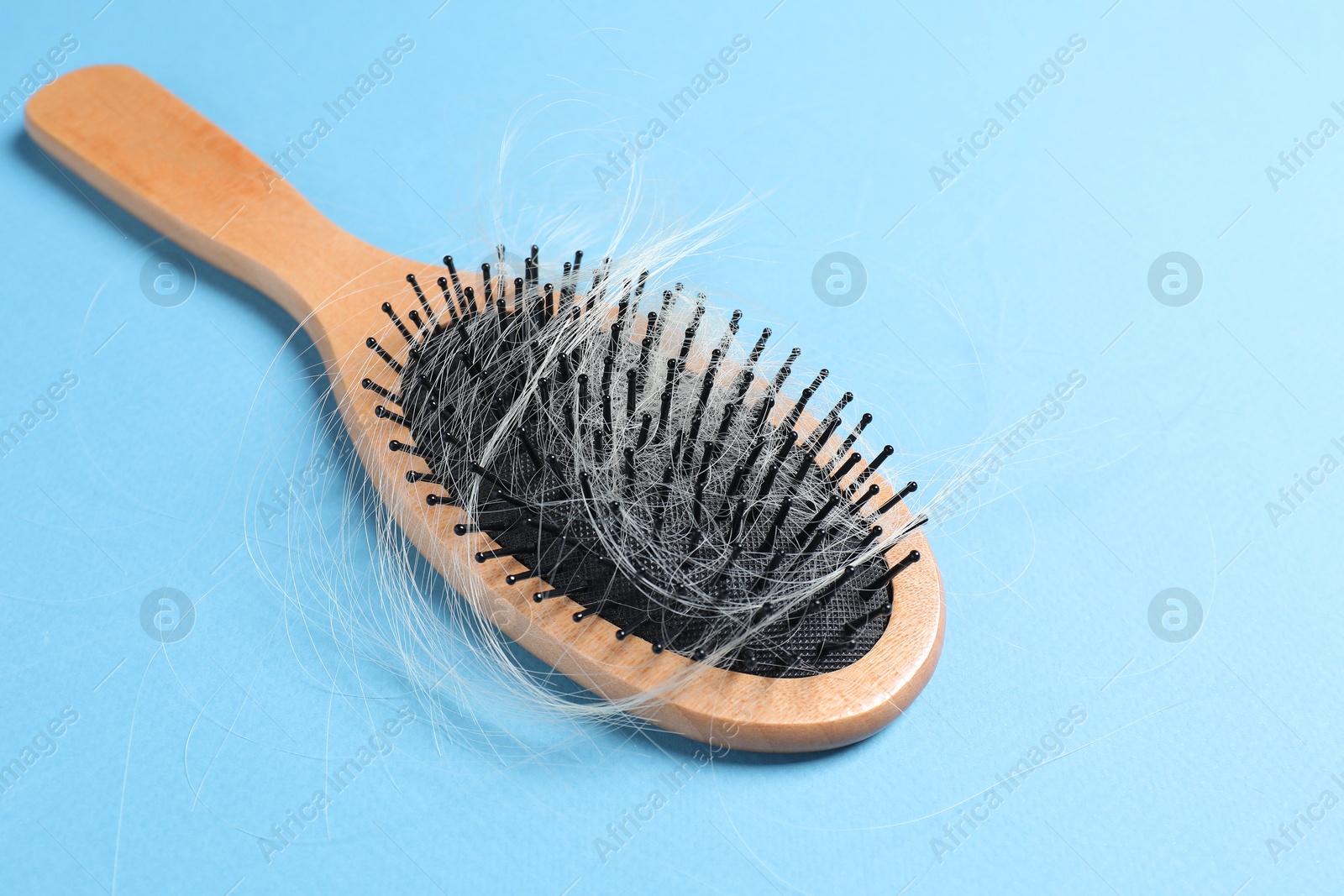 Photo of Wooden brush with lost hair on light blue background